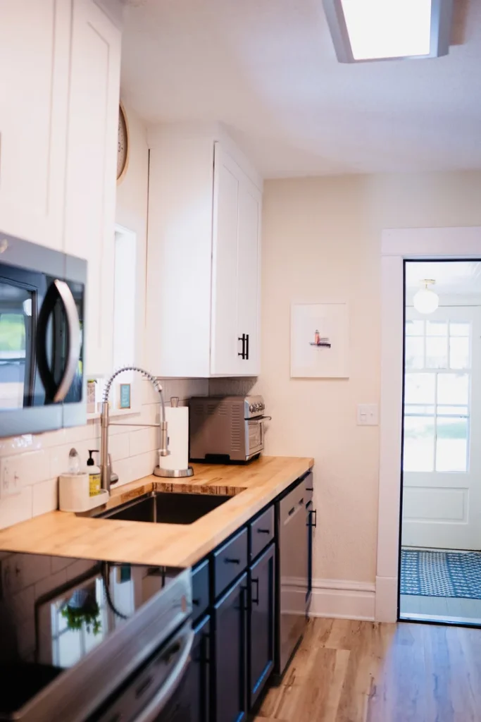 Kitchen with a wooden countertop, white cabinets, black lower cabinets, a stainless steel microwave, and a window over the sink.