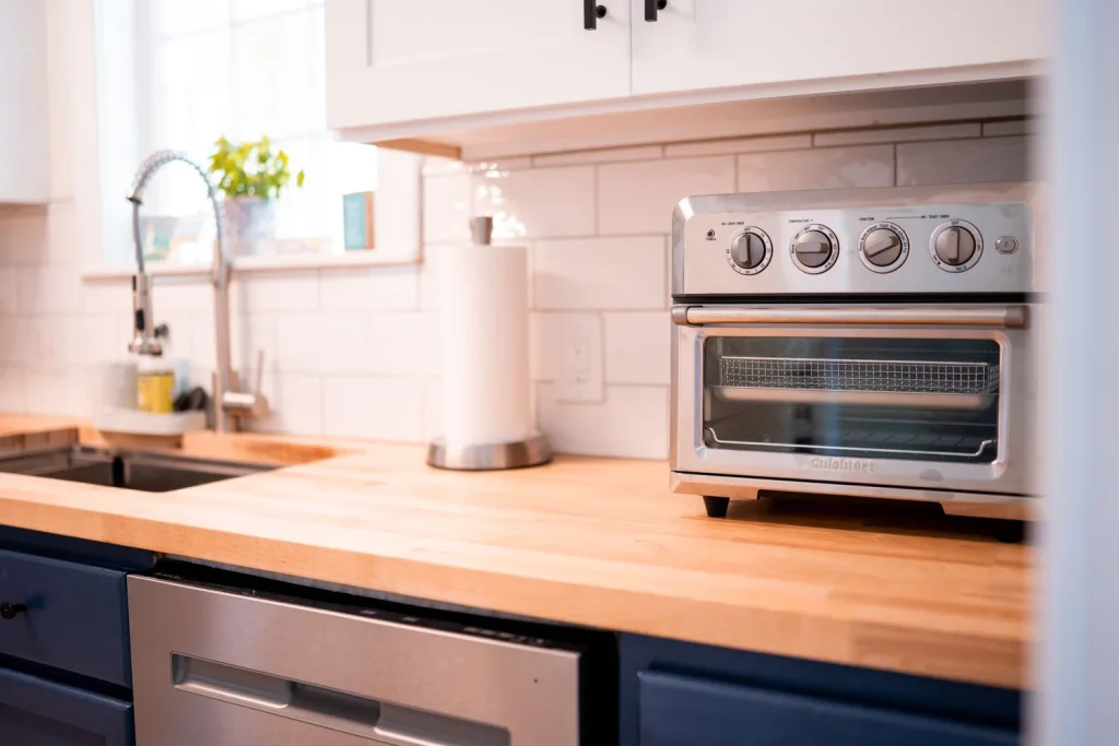 Kitchen countertop with a stainless steel toaster oven, paper towel roll, kitchen sink, and potted plant.