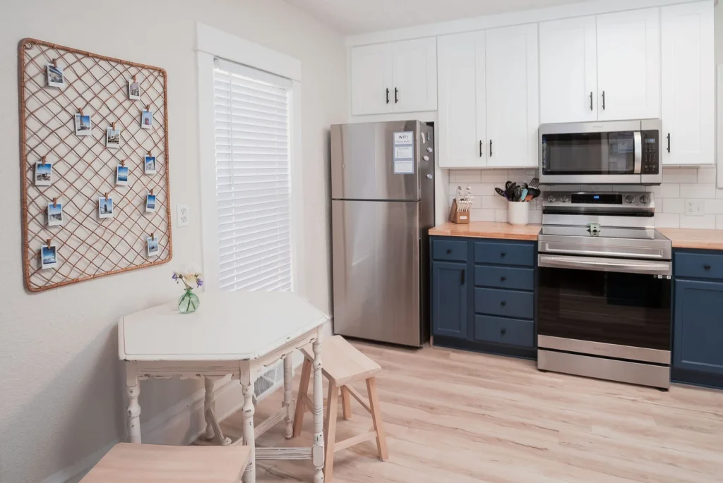 Kitchen with white cabinets, stainless steel refrigerator and oven, wooden countertops, blue lower cabinets, and a small white table with chairs.